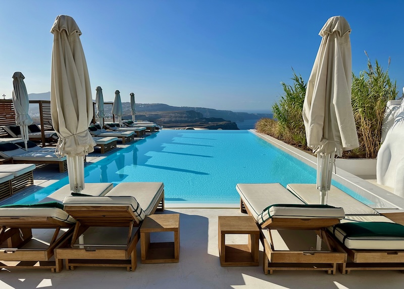 Infinity pool lined with sunbeds and umbrellas overlooking the caldera at Katikies Garden in Santorini.