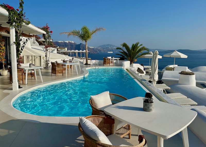A freeform infinity pool on a classy terrace with bougainvillea and palm trees at Katikies hotel in Santorini.