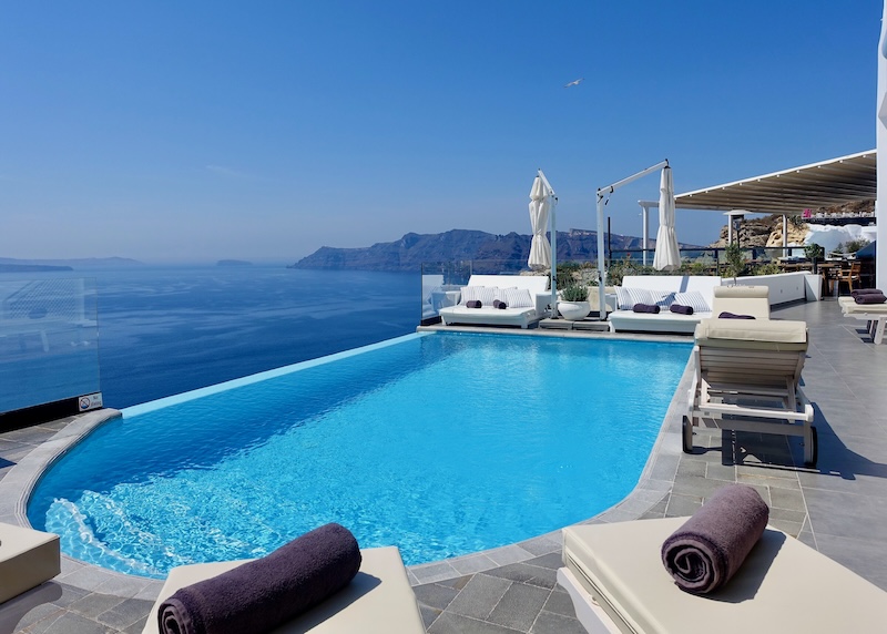 Infinity pool with sunbeds all around it and a caldera view at Santorini Secret in Oia.
