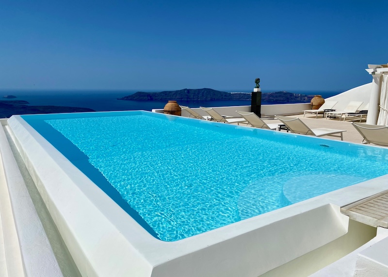 Infinity pool and sun terrace overlooking the caldera toward the volcanoes and Thirassia Island at Tsitouras Collection in Santorini.