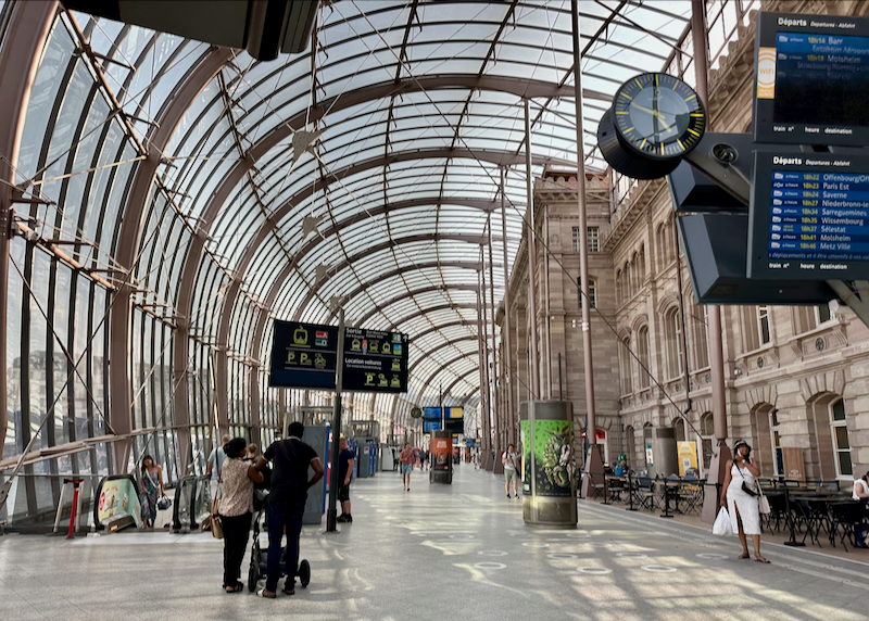 Travelers inside the light-filled atrium of Gare Strasbourg in Strasbourg, France