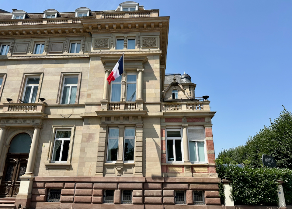 Exterior of a classically elegant stone hotel, flying a French flag