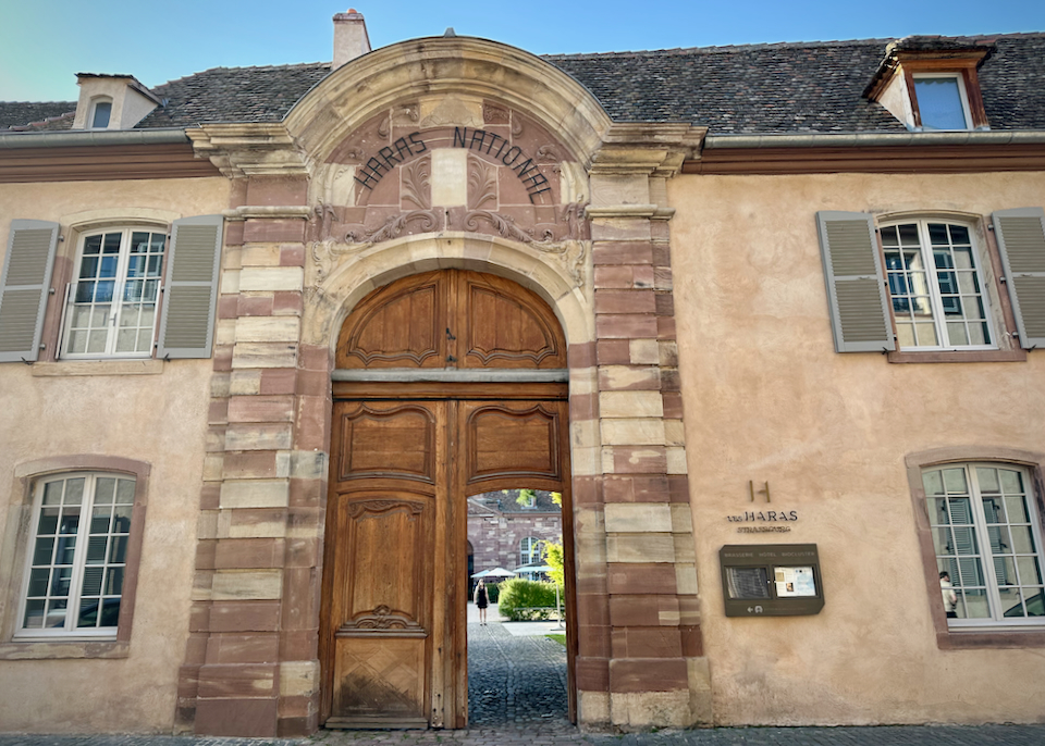 Large wooden door in a stone wall, open to show a sunny courtyard within