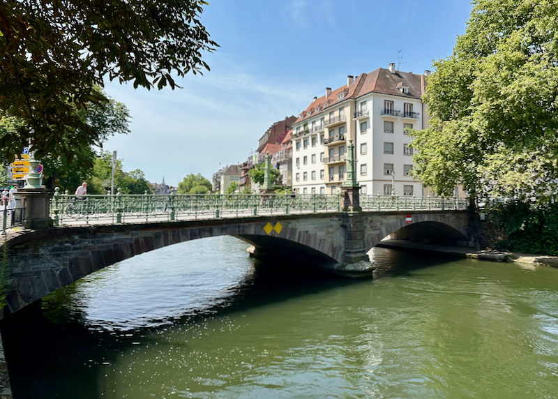 Small and picturesque bridge spanning a small river, with French buildings in the background