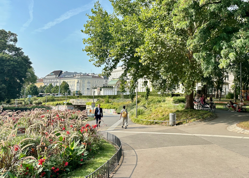 People walk along curved paths past flowering gardens in a Vienna park