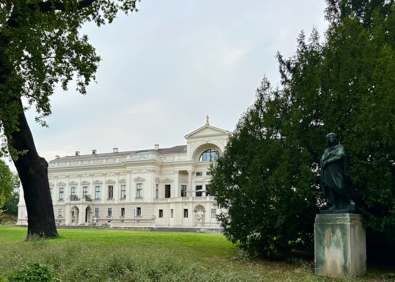 View past trees and a small statue to a grand white palace building