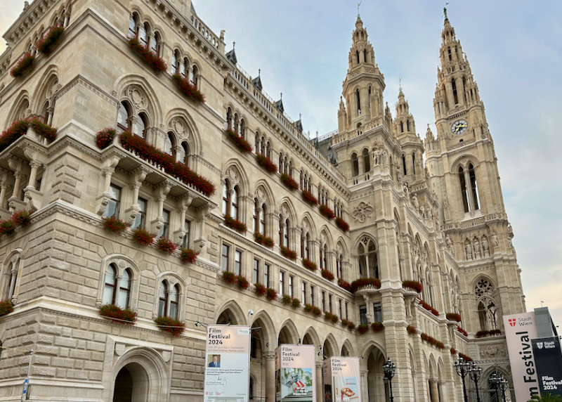 View looking up at a gothic town hall with red flowers adorning its many windows