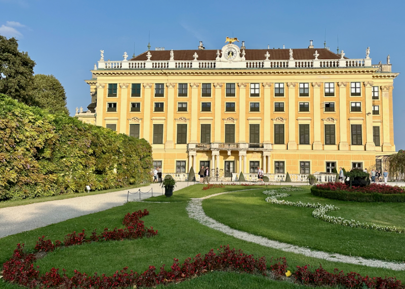 Manicured gardens in front of an ornate yellow palace building