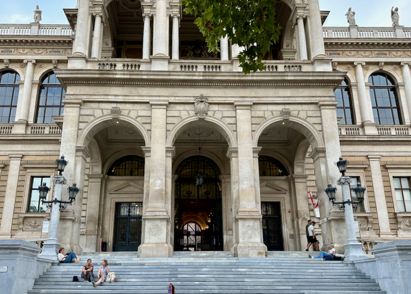 Students sit on the steps of the grand entrance to the University of Vienna