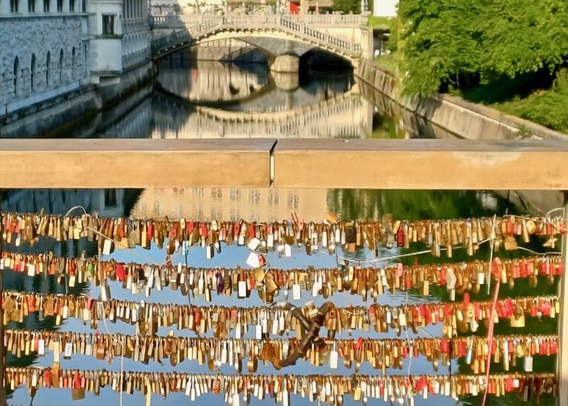 hundreds of paddle locks line a railing over a river.