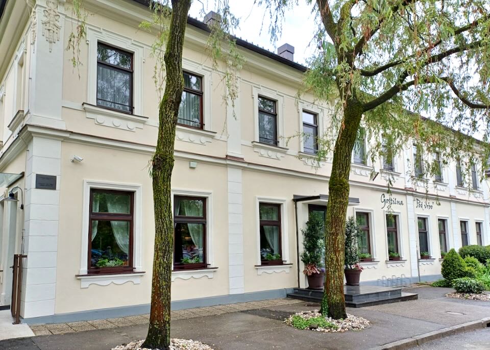 A pale yellow hotel with two trees in front.