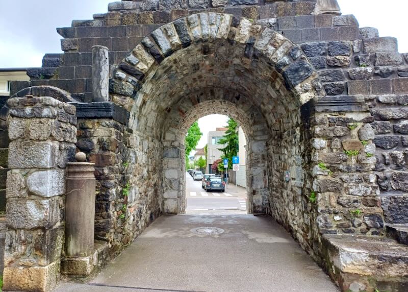 Old stone walls create an arched passage to a road.