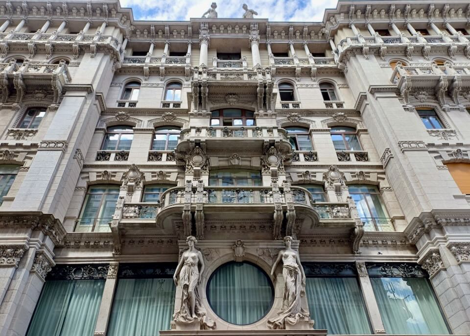 The face of a building has sculptures of women and intricate balconies.