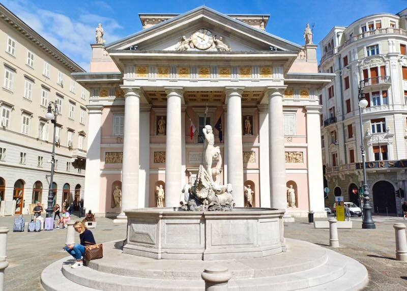 A woman sits on the steps that lead to a fountain.