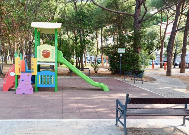 A playground sits on a slab of stone surrounded by trees.