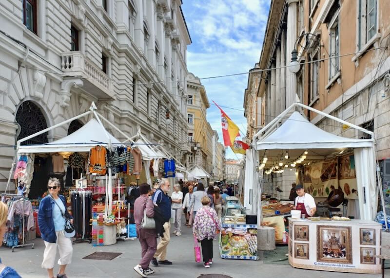 People walk through a street market between two large buildings.