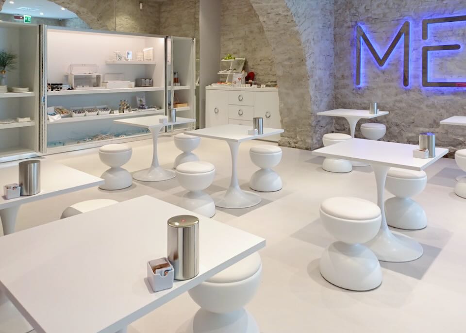 White tables and white stools sit in a stone room.