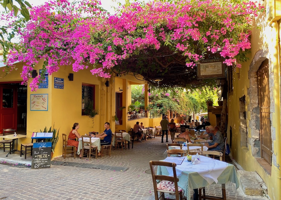 A restaruant with outdoor tables under a large bougainvillea in Chania.