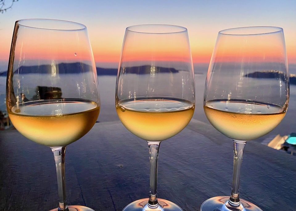 Three glasses of white wine reflecting the colors of the sunset at Athenian House in Imerovigli.