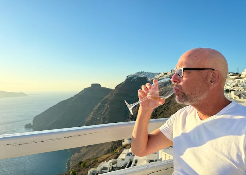 Santorini Dave (me) drinking wine with a view of the Santorini caldera.
